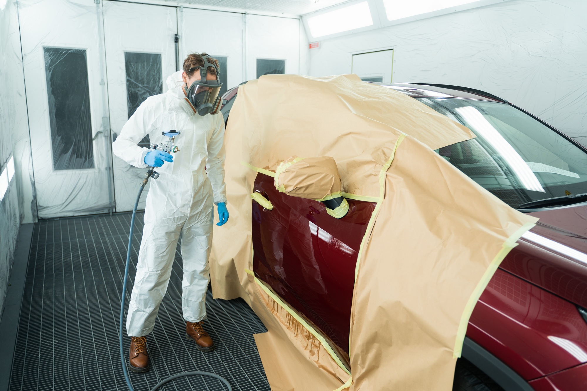 Auto painter with spray gun in car painting booth